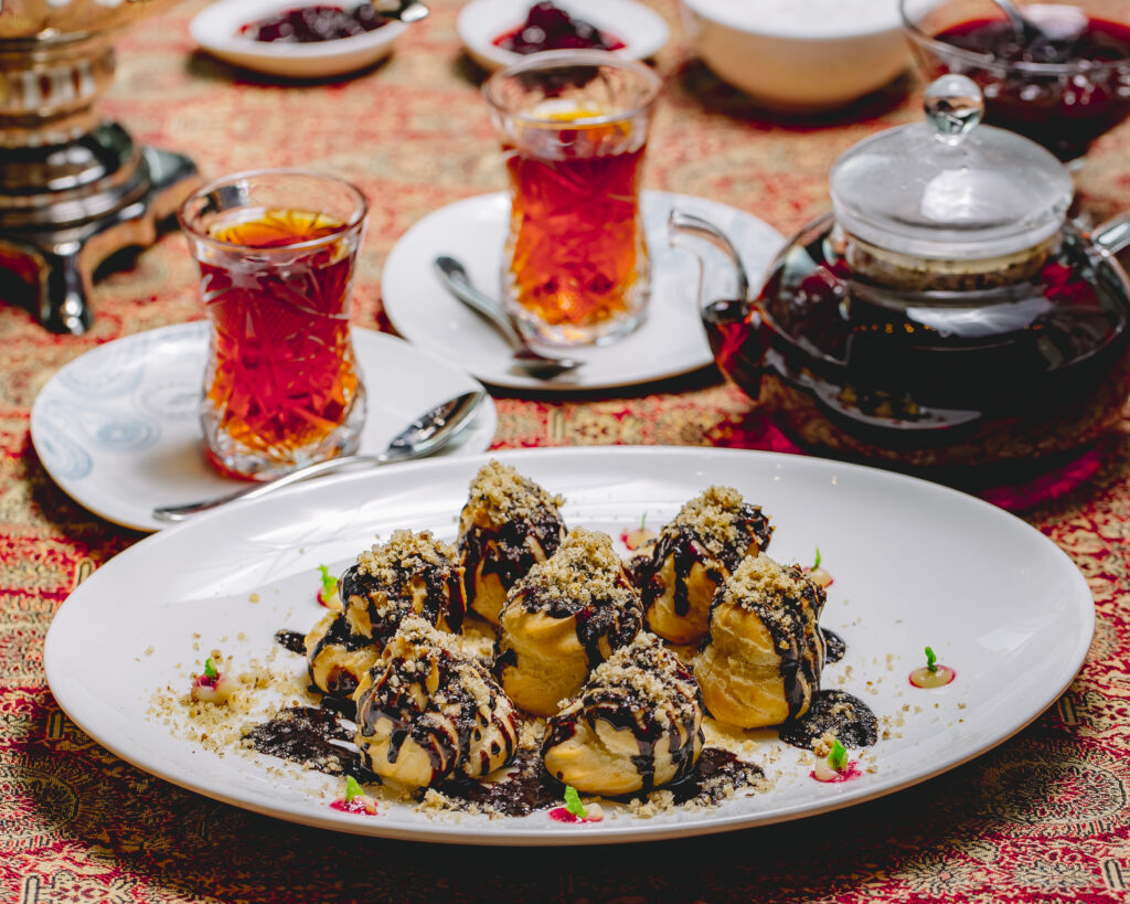 Front view dessert profiteroles with chocolate icing and grated nuts with two glasses of tea